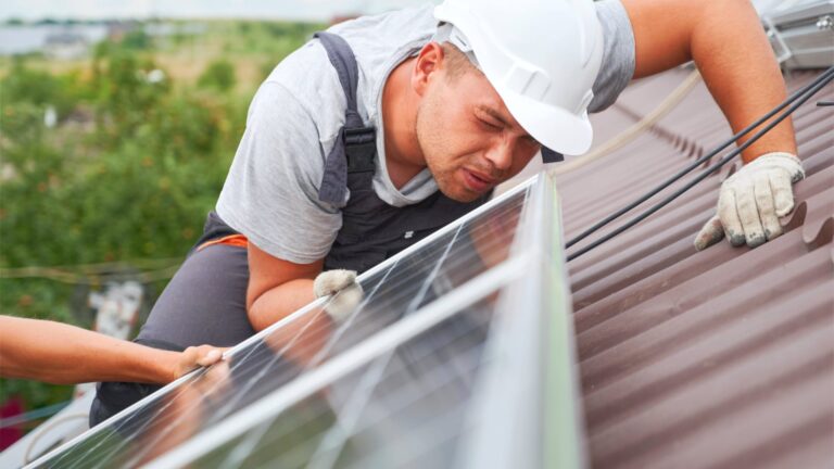 Arbeiter eines regionalen Fachbetriebs installiert Solarmodule einer PV-Anlage auf einem Hausdach.